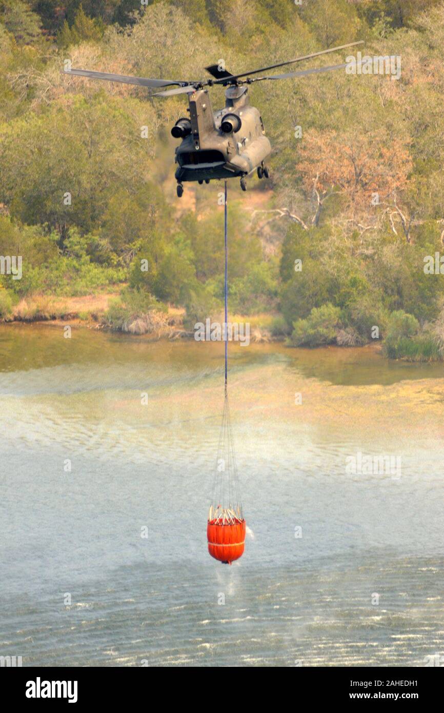 Un' antenna la mandata di acqua la benna piena di acqua sotto un CH-47 elicottero Chinook da 2-149th, TXARNG, sorge da un lago o fiume per tornare a un tripudio nei pressi di immobili residenziali, vicino Bastrop Texas, Sett. 6, 2011. Texas National Guard per equipaggi lanciato al di fuori dell'esercito di Austin Aviation Facility per la lotta contro gli incendi selvaggi. Essi sono parte di un interagenzie di risposta che include U.S. Dipartimento dell'Agricoltura, Servizio di Foresta che quando è necessario volare missioni di osservazione per antenna diretta wildfire operazioni di combattimento. Dal 1975, il Dipartimento di Agricoltura e il ministero degli Interni hanno avuto un interag Foto Stock