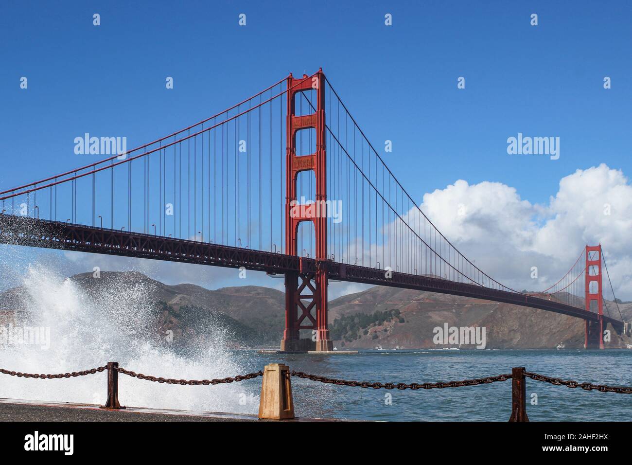 Onde che si infrangono sulla al terrapieno con arancio internazionale Golden Gate Bridge in background in San Francisco, Stati Uniti d'America Foto Stock