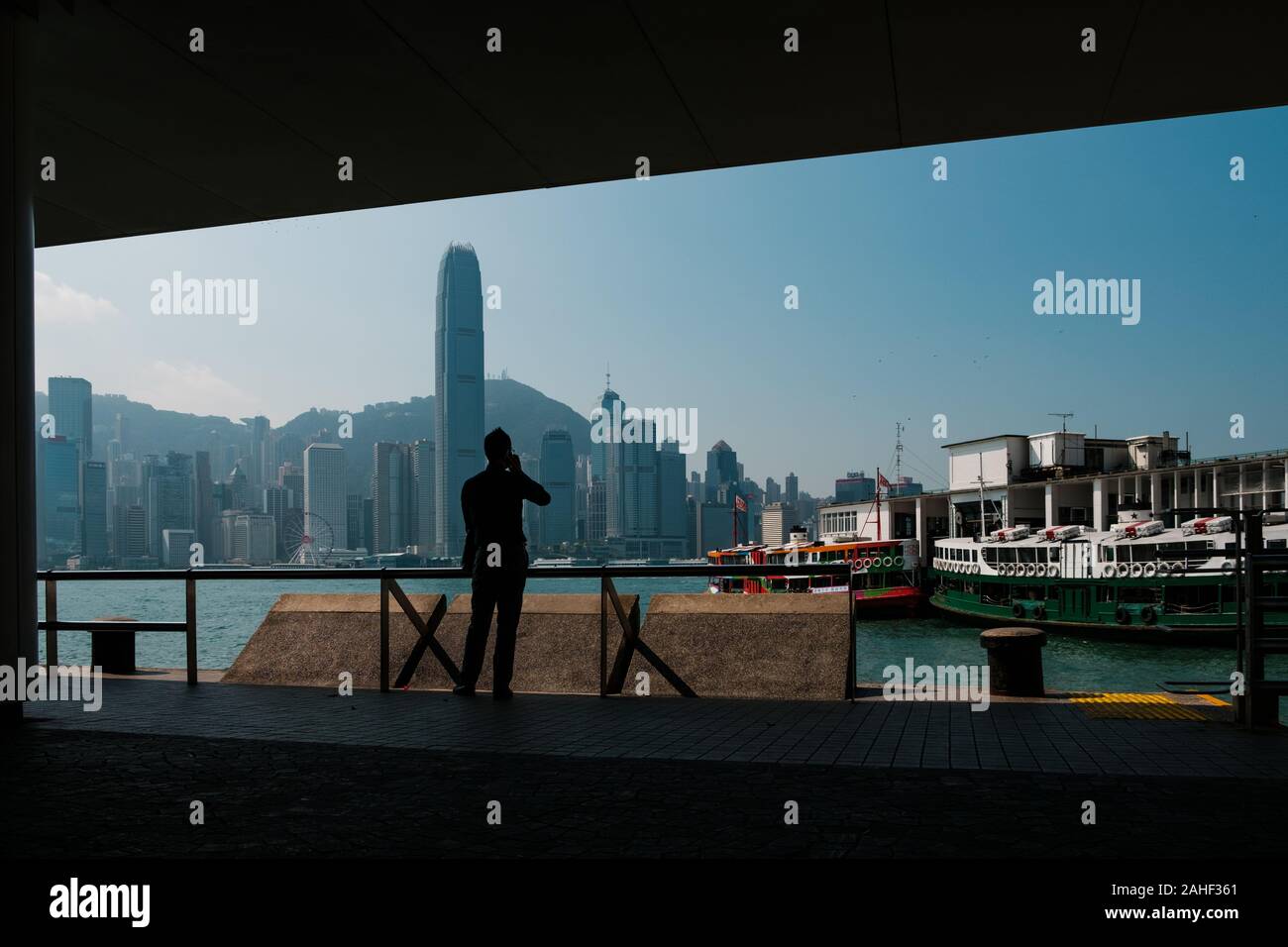 Hong Kong Cina - Novembre 2019: Silhouette di un uomo sul telefono mobile guardando a Tsim Sha Tsui Molo Star Ferry e dell'Isola di Hong Kong skyline Foto Stock