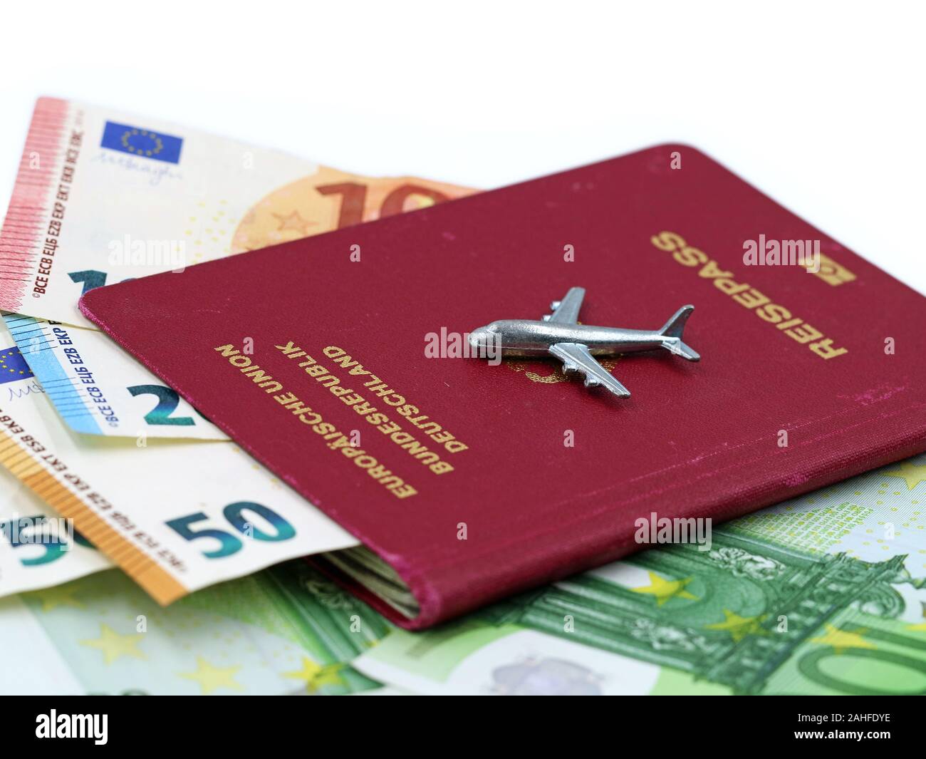 Aeroplano in miniatura sul passaporto tedesco con le banconote in euro all'interno su sfondo bianco, spazio di copia Foto Stock