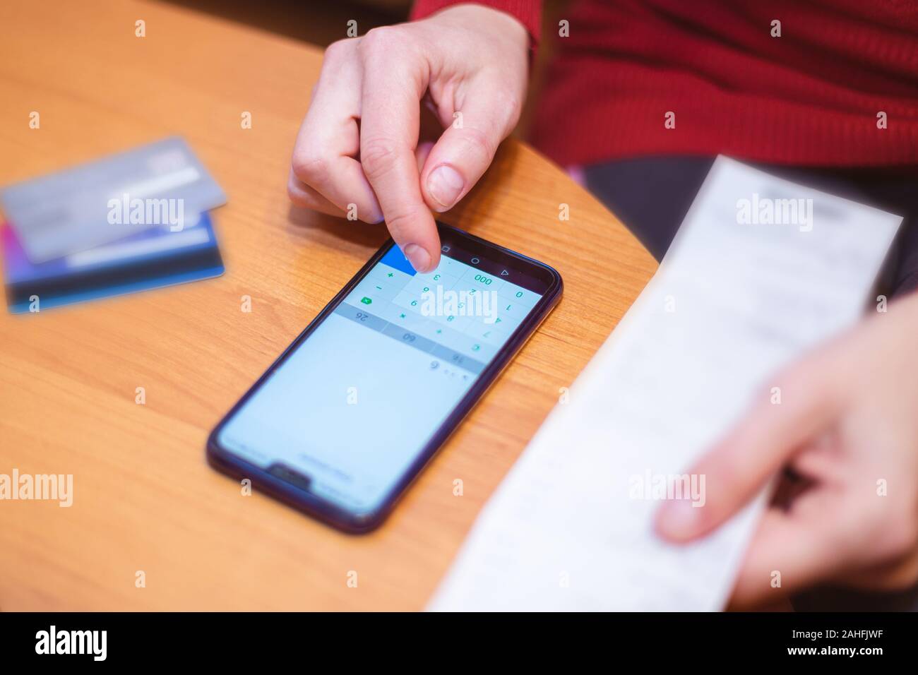 Persona che calcola il totale degli acquisti dalla ricevuta fiscale sul suo telefono cellulare su una tavola. Concetto di contabilità di bilancio di cassa Foto Stock