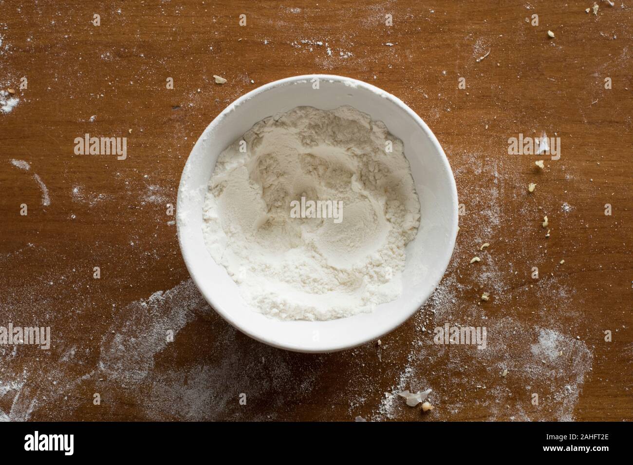 Ciotola bianco parzialmente riempito con farina, seduto su di una cucina in legno superficie che è stata leggermente spolverata di farina Foto Stock