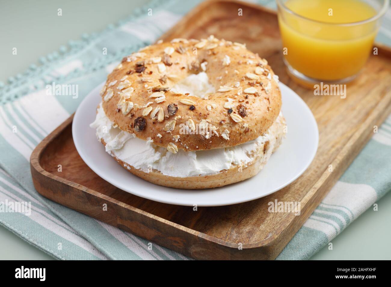 Sandwich di bagel con formaggio morbido e un bicchiere di succo di arancia su un vassoio in legno Foto Stock