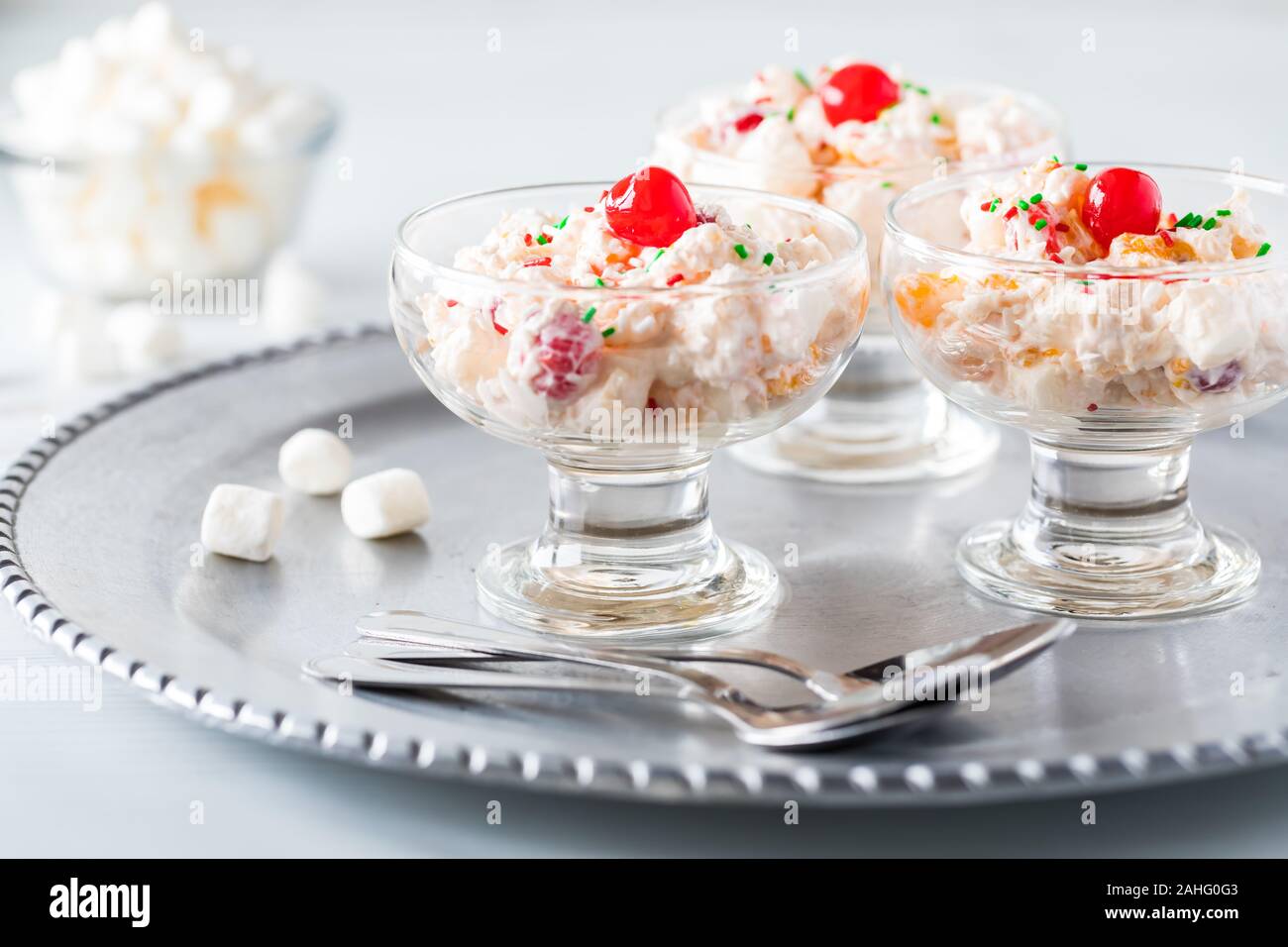 Una chiusura in vetro piatti da dessert riempito con insalata di ambrosia e rabboccato con ciliegie al maraschino e una piccola ciotola di mini marshmallows. Foto Stock