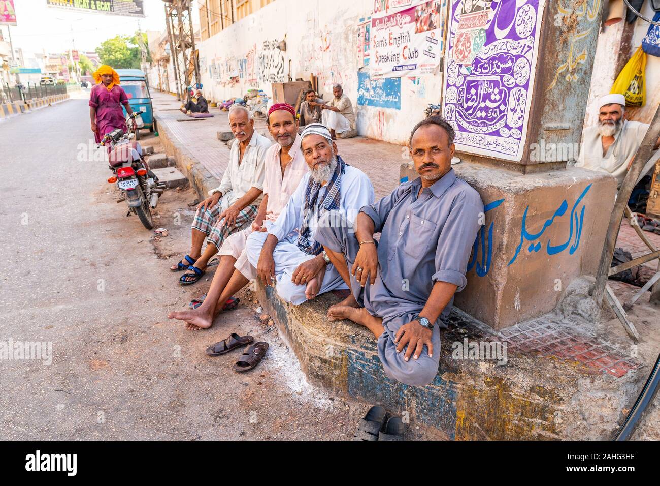 Hyderabad vista pittoresca di quattro seduta con gioia vecchio ragazzi pakistani in corrispondenza di una strada su una soleggiata cielo blu giorno Foto Stock