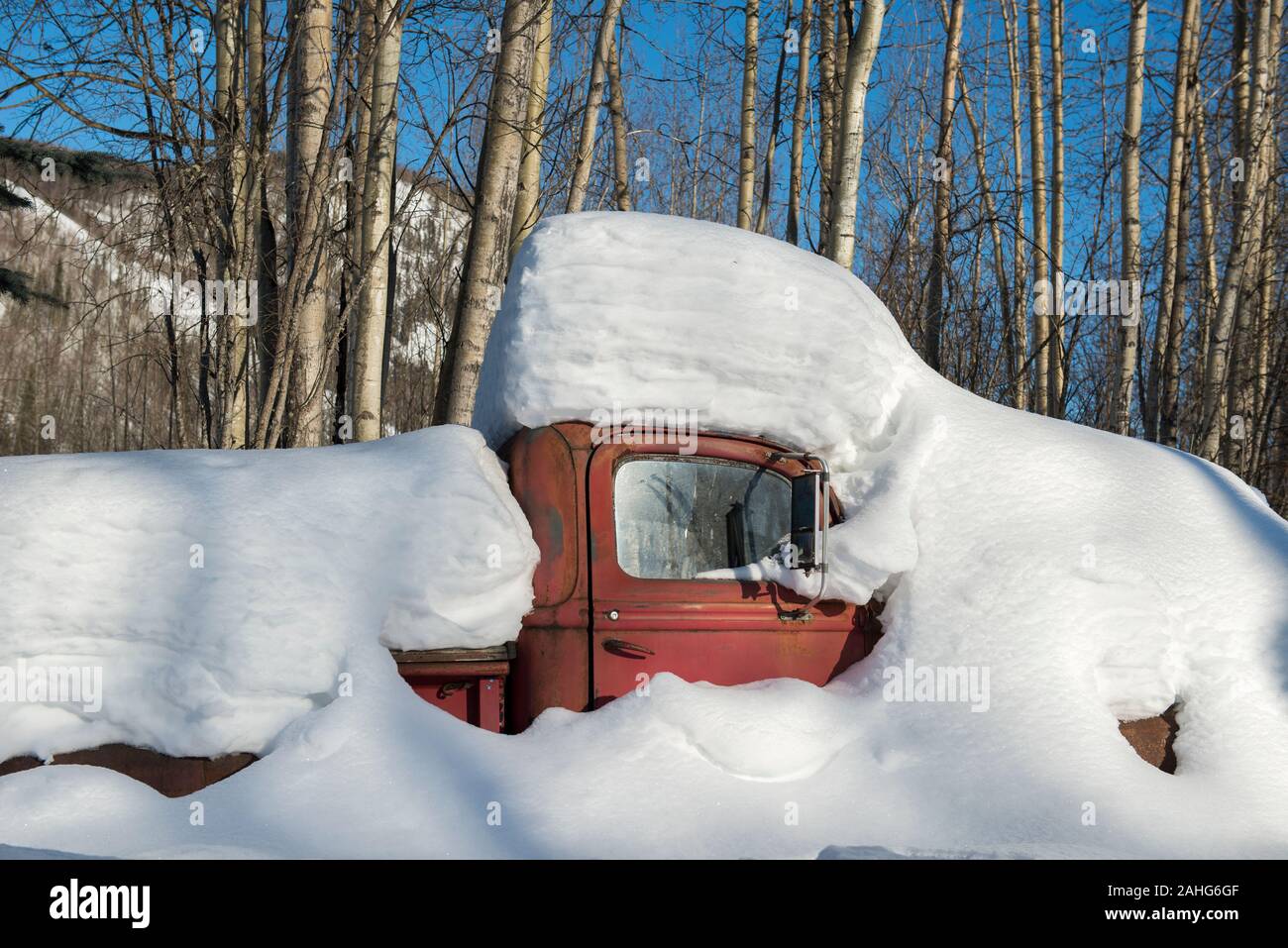 Un vecchio camion rosso sepolto nella neve in una giornata di sole nella foresta di Alaskan Foto Stock