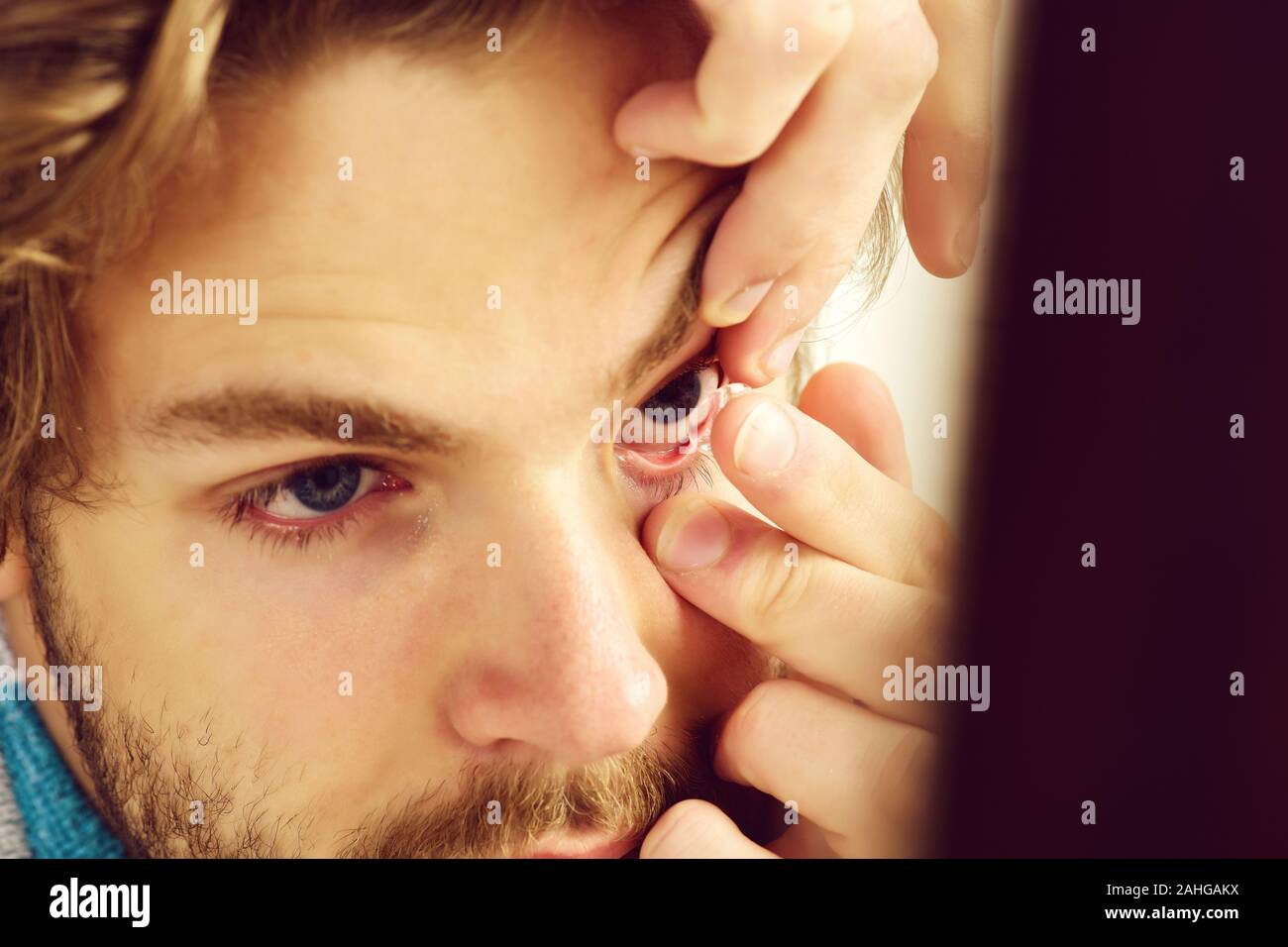 Uomo con la barba e gli occhi blu mette le lenti a contatto su, vicino. Guy detiene una lente correttiva sul suo dito, il fuoco selettivo. Salute, oftalmologia e concetto di visione Foto Stock