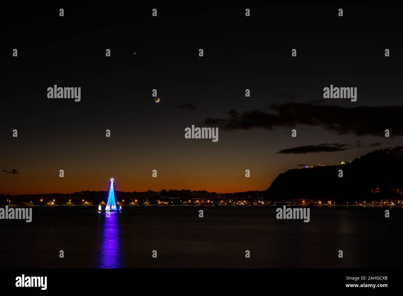 Bacoli Napoli, 27 dicembre 2019. Un albero illuminato al centro del lago con una fetta di luna sullo sfondo. Foto Stock