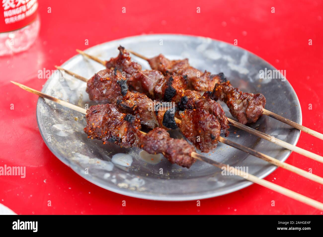 Quattro spiedini di agnello alla griglia, serviti su un piatto e pronti a mangiare. Cibo tipico dello Xinjiang - come cibo di strada o servito in ristoranti. Foto Stock