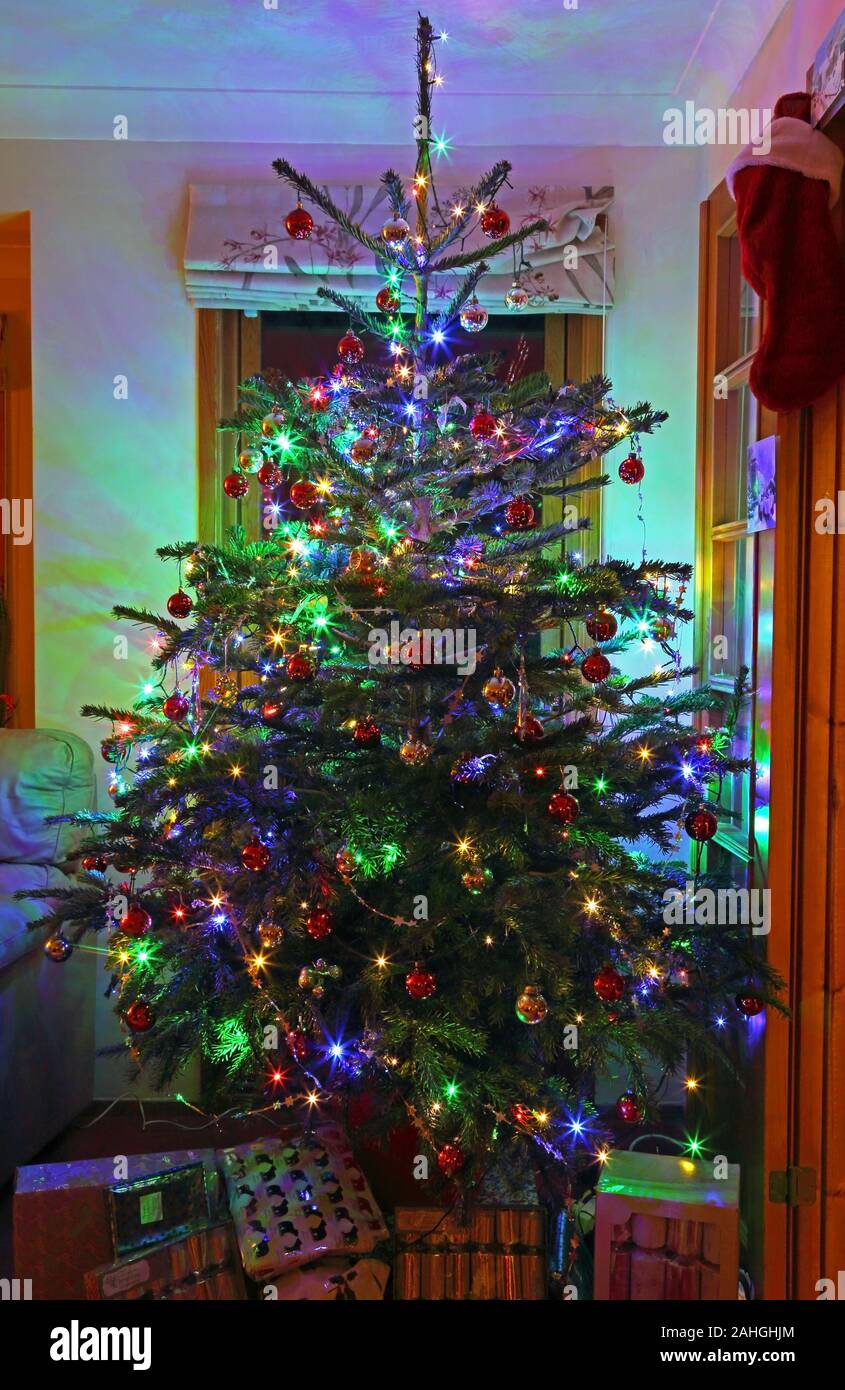 Albero di Natale decorato con baubles, tinsel e le luci di Natale con regali di Natale intorno alla base, Surrey, England, Regno Unito Foto Stock