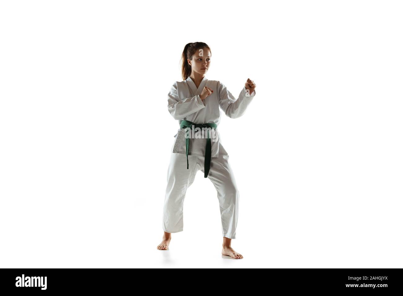 Fiducioso junior in kimono la pratica di combattimento a mani nude, arti marziali. Femmina e giovane guerriero mongolo con cintura verde della formazione su bianco di sfondo per studio. Concetto di stile di vita sano, sport, azione. Foto Stock