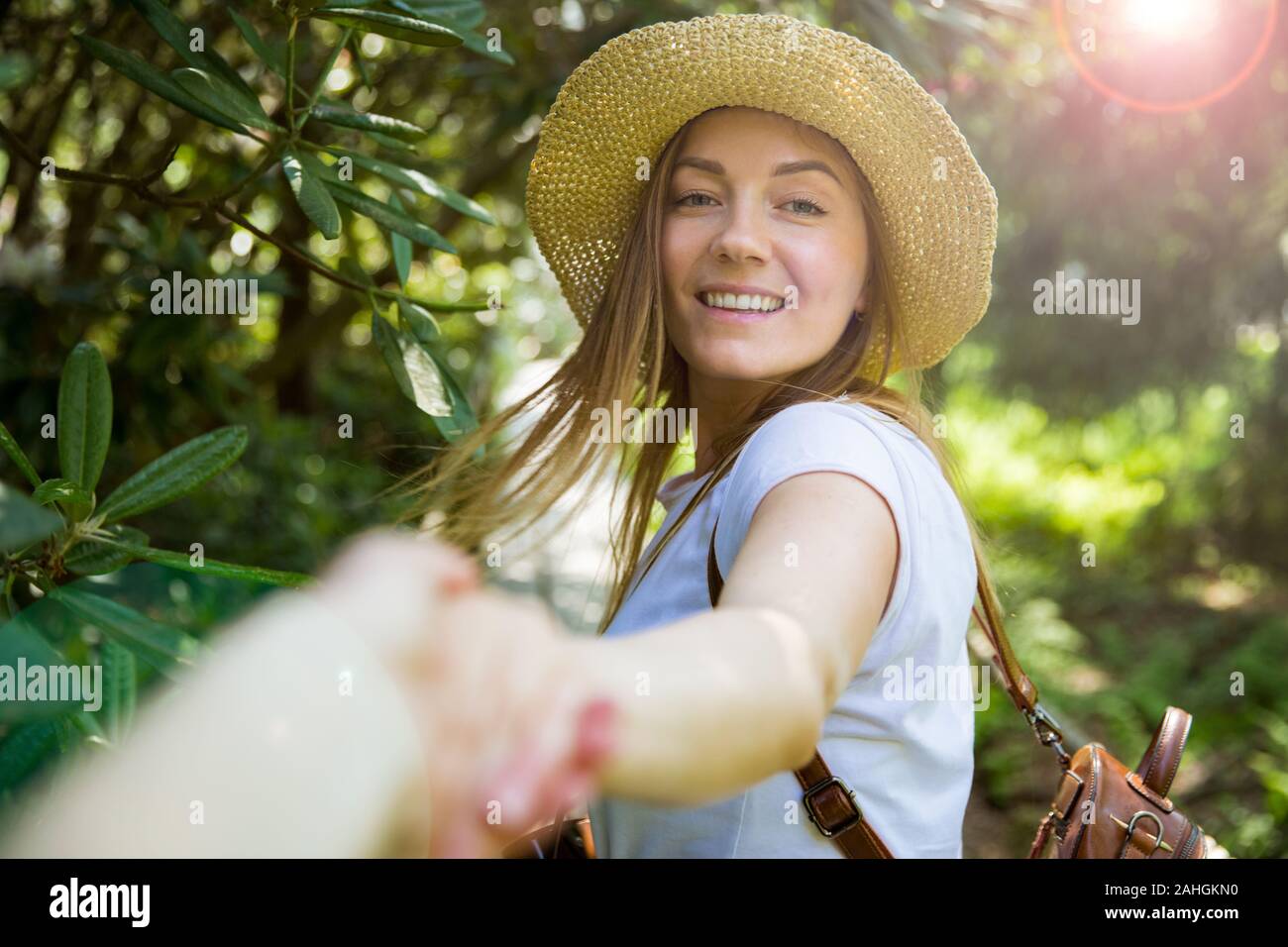 Bella donna in cappello di paglia viaggio nella foresta tropicale, camminando lungo il sentiero di legno, che conduce il suo partner. Turistico con zaino. Seguimi il concetto. Foto Stock
