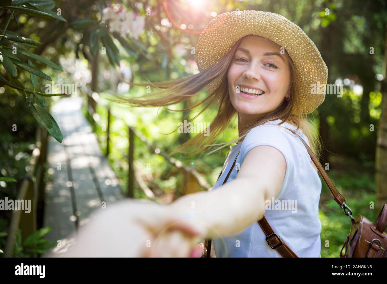 Bella donna in cappello di paglia viaggio nella foresta tropicale, camminando lungo il sentiero di legno, che conduce il suo partner. Turistico con zaino. Seguimi il concetto. Foto Stock
