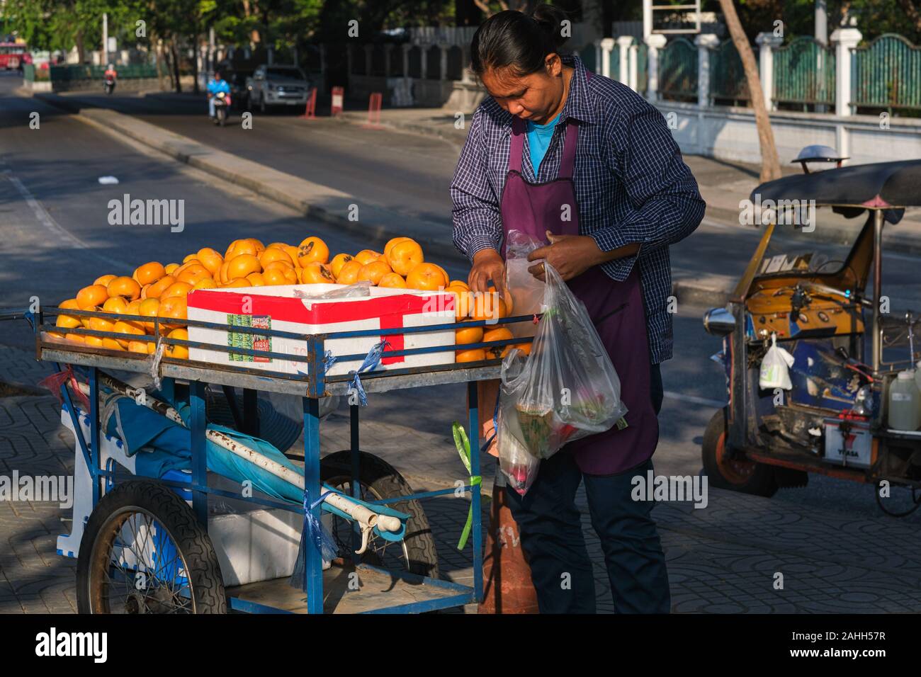 Un mobile fornitore di frutta a Bangkok, Thailandia, con il suo carrello pieno di cachi (persimons) Foto Stock