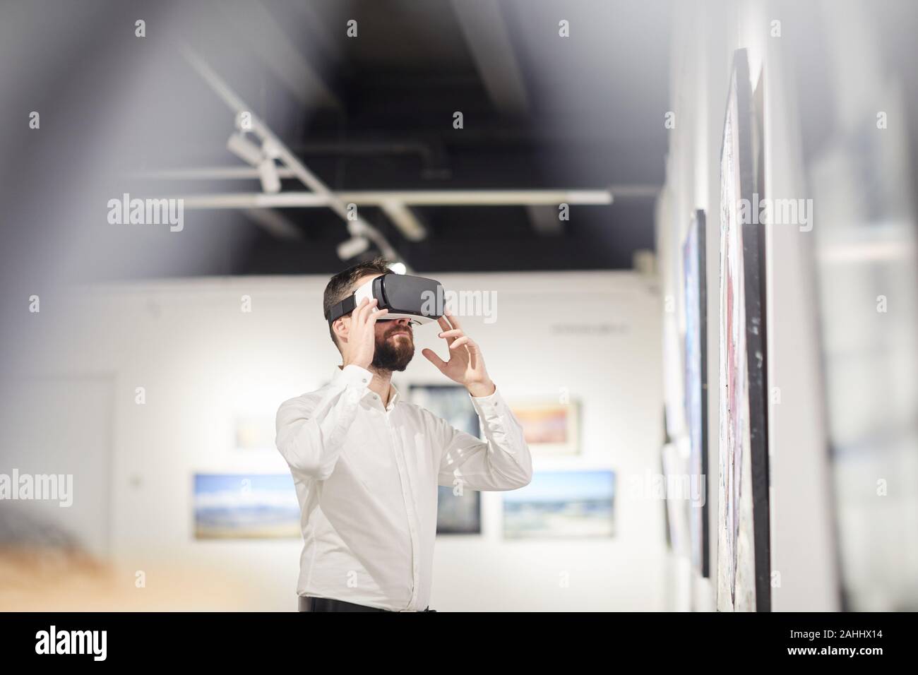 Vista laterale verticale del moderno uomo barbuto che indossa VR marcia mentre godendo coinvolgente esperienza durante il periodo di esposizioni in galleria d'arte, spazio di copia Foto Stock