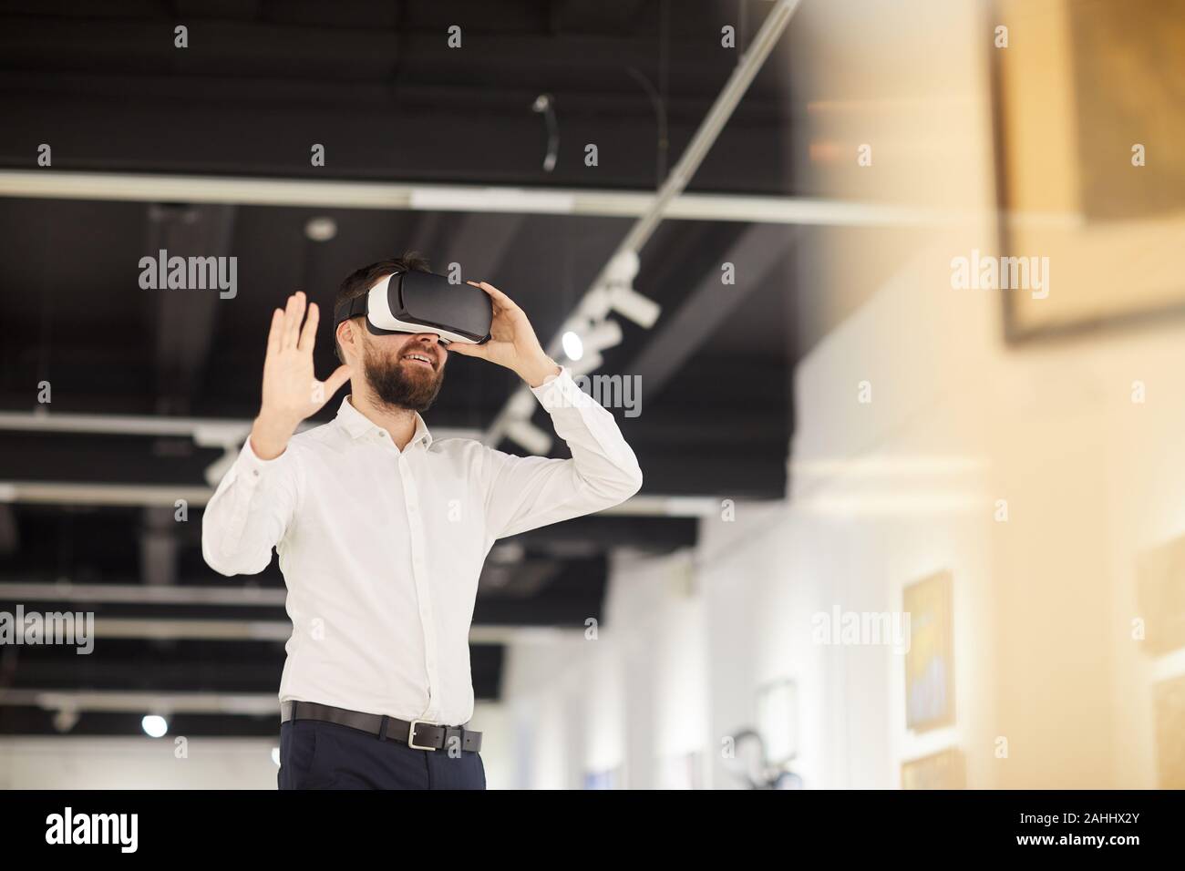 Vita ritratto di moderno uomo barbuto che indossa VR marcia mentre godendo coinvolgente esperienza durante il periodo di esposizioni in galleria d'arte, spazio di copia Foto Stock