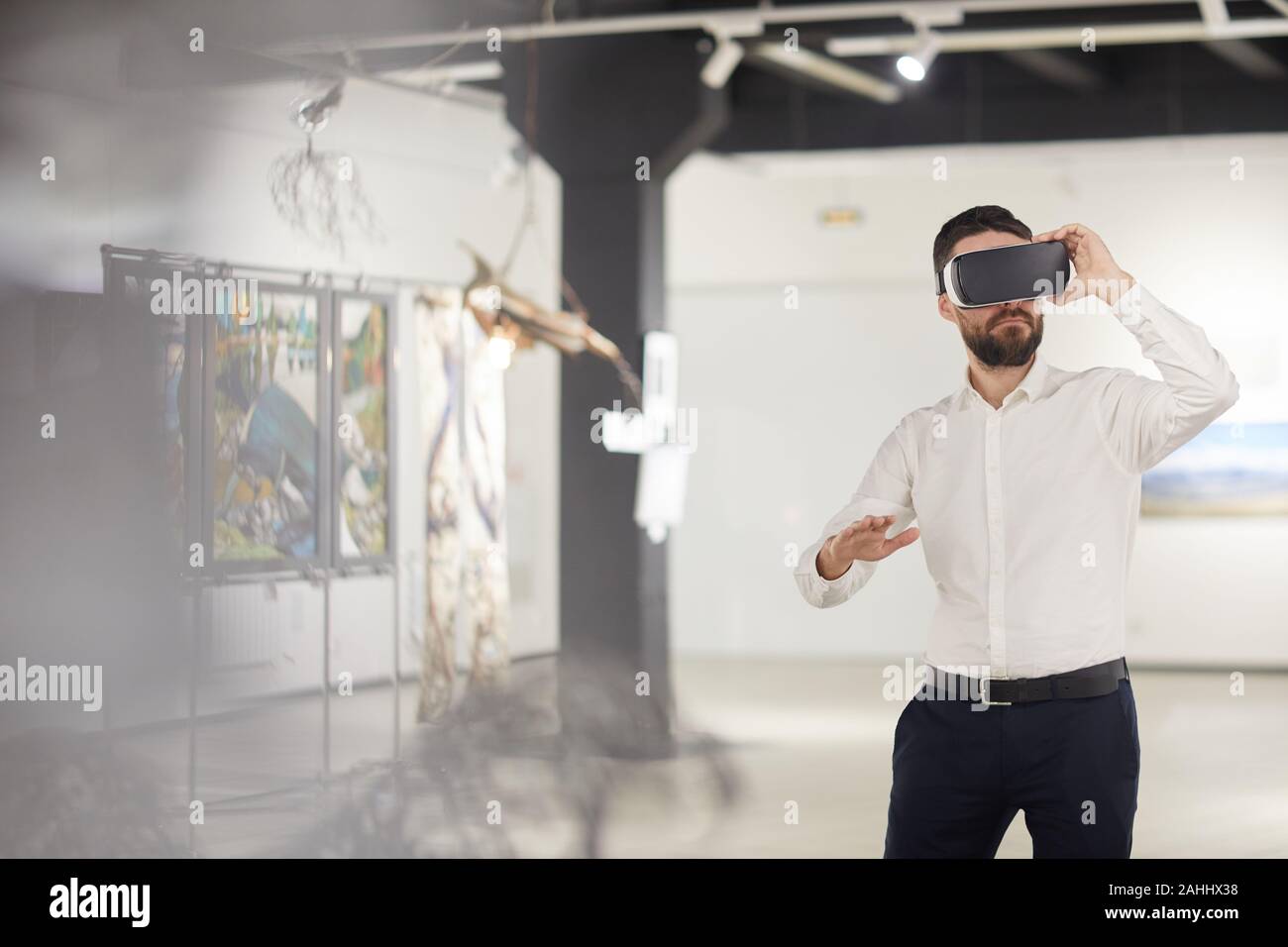 Ritratto di moderno uomo barbuto che indossa VR marcia mentre godendo coinvolgente esperienza durante il periodo di esposizioni in galleria d'arte, spazio di copia Foto Stock