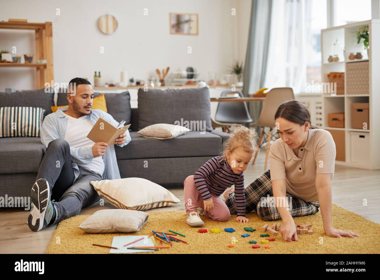 A piena lunghezza Ritratto di felice famiglia moderna giocando con graziosi bambina in accogliente soggiorno interno, spazio di copia Foto Stock