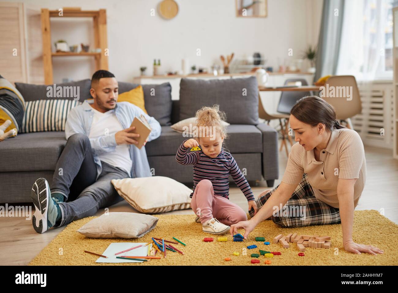 A piena lunghezza ritratto della moderna mixed-gara famiglia giocando con graziosi bambina in accogliente soggiorno interno, spazio di copia Foto Stock