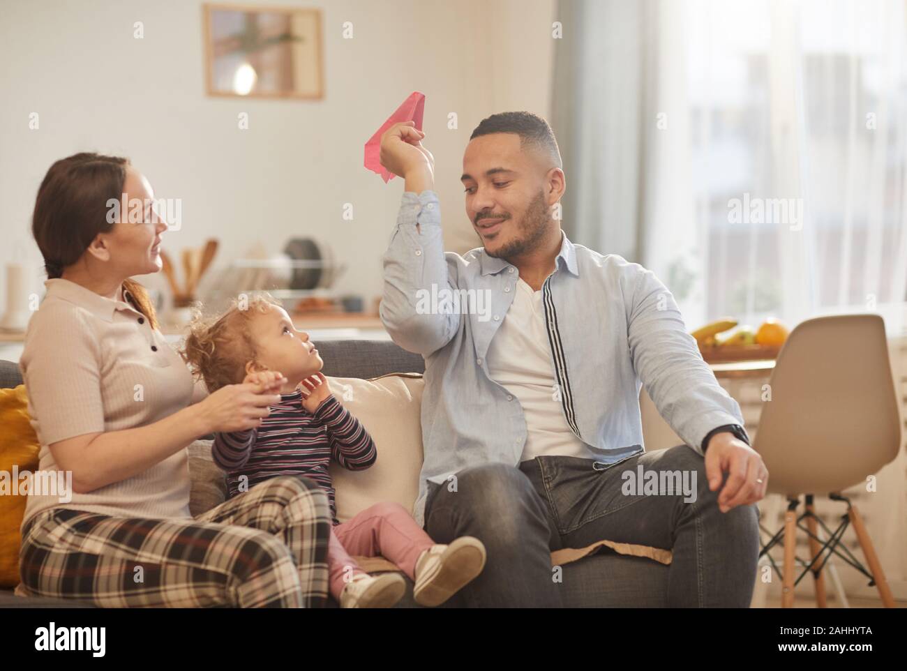 Dai toni caldi ritratto di felice famiglia moderna giocando con graziosi bambina in casa accogliente interno, spazio di copia Foto Stock