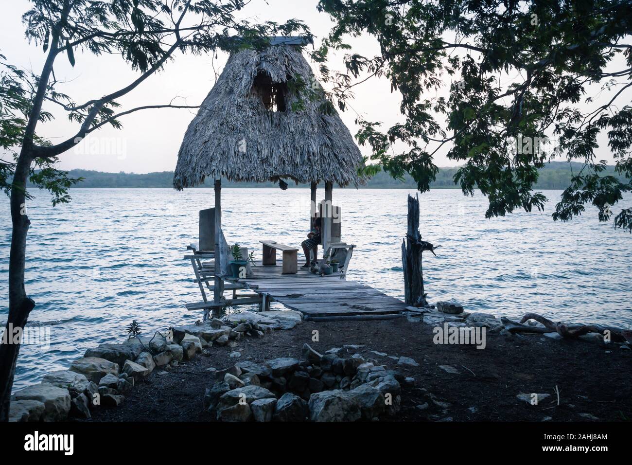 Piccolo dock con tetto in foglia di palma a lago Salpeten dopo il tramonto, vicino a El Remate, Peten, Guatemala Foto Stock