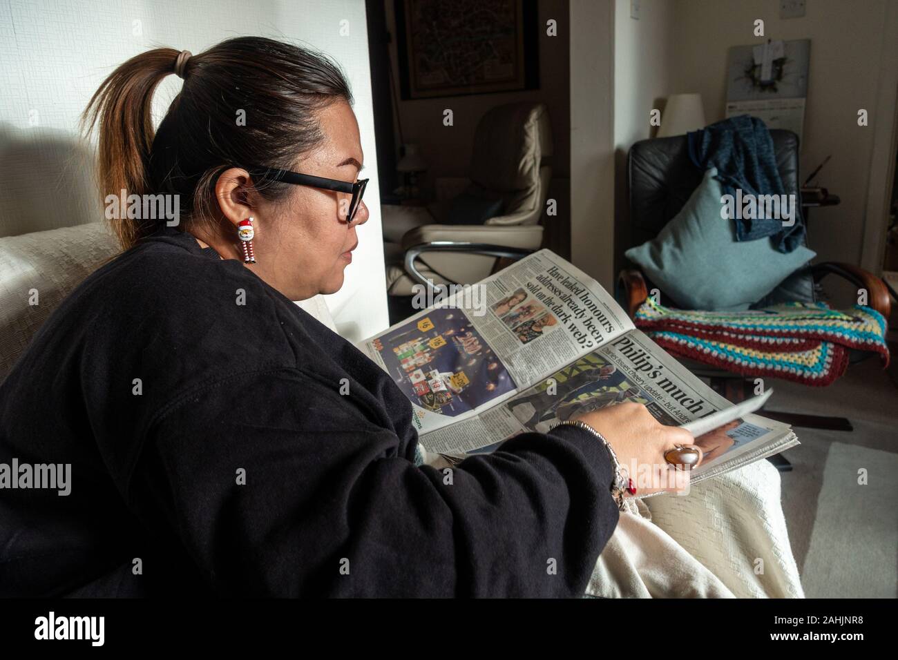 Una donna si siede sul divano e legge un giornale. Foto Stock