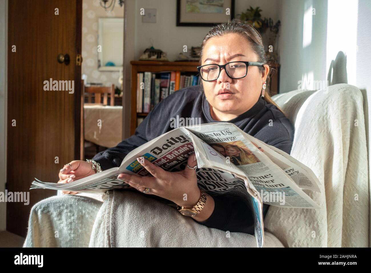 Una donna si siede sul divano e legge un giornale. Foto Stock