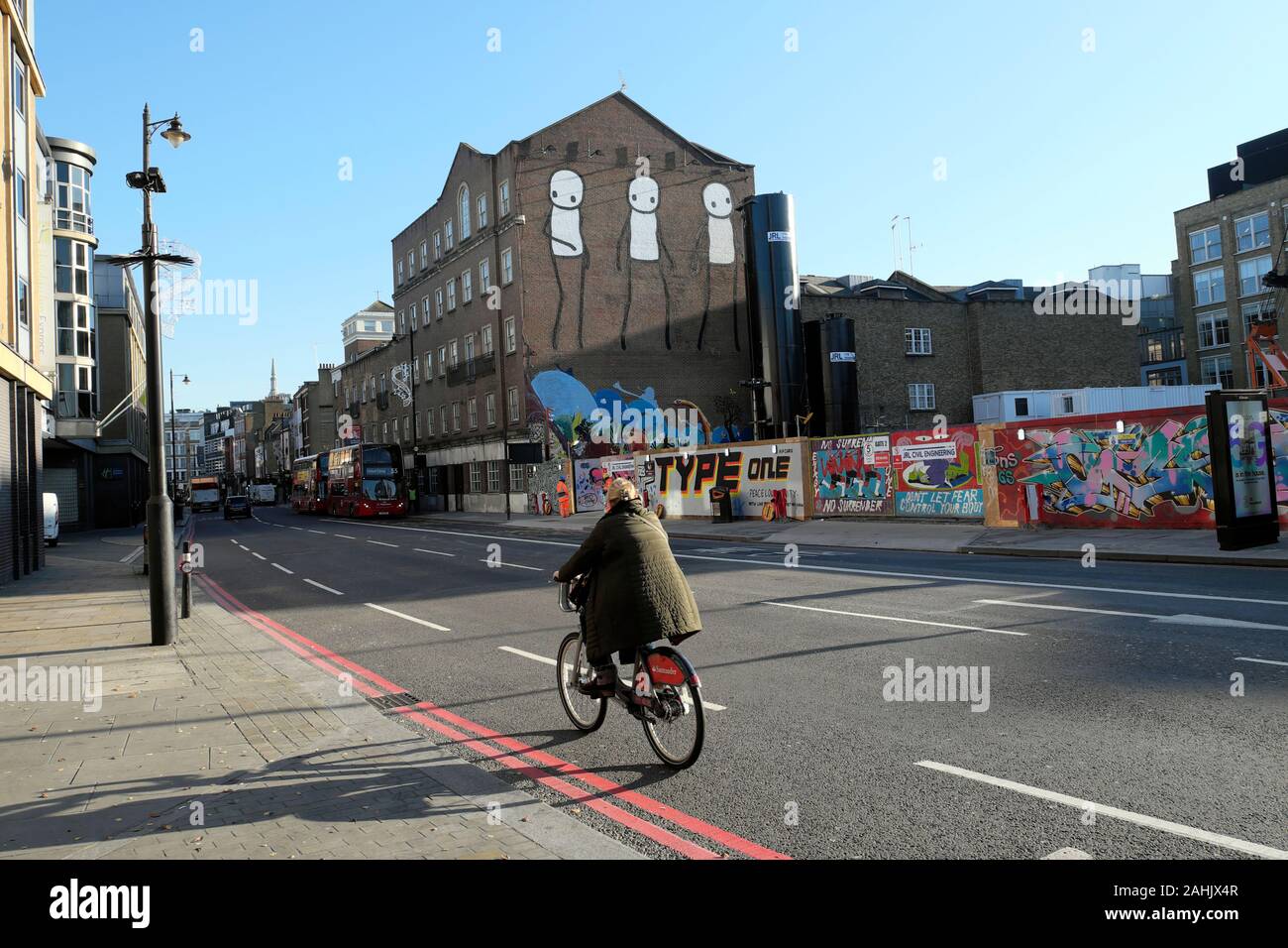 Ciclista in sella a Santander regime noleggio bici da strada Stik arte murale e graffiti su costruzione palizzata su Old Street London EC2 UK KATHY DEWITT Foto Stock