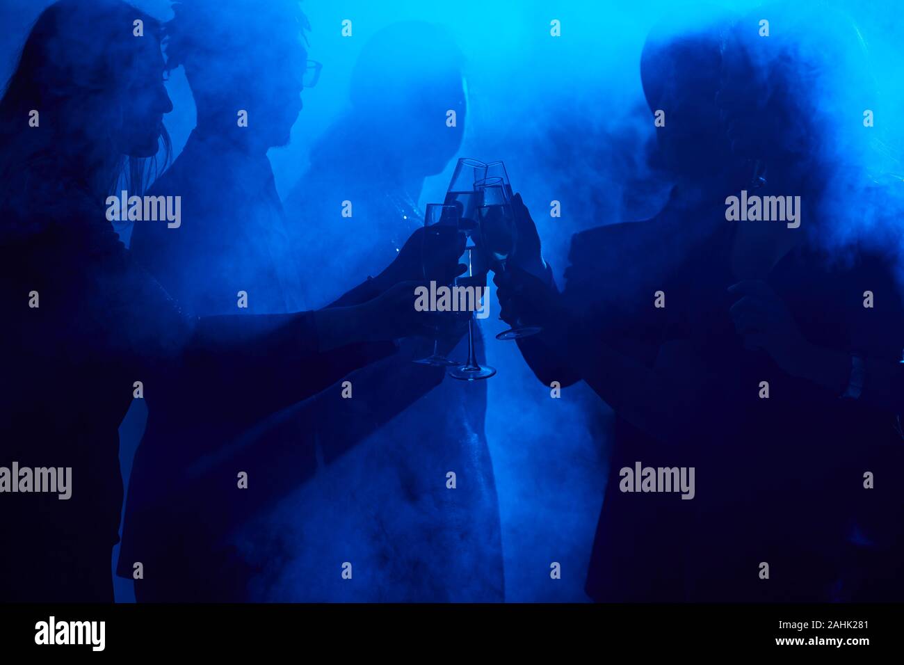 Sagome scure dei giovani tintinnanti bicchieri di champagne in smoky night club mentre si celebra a parte, spazio di copia Foto Stock