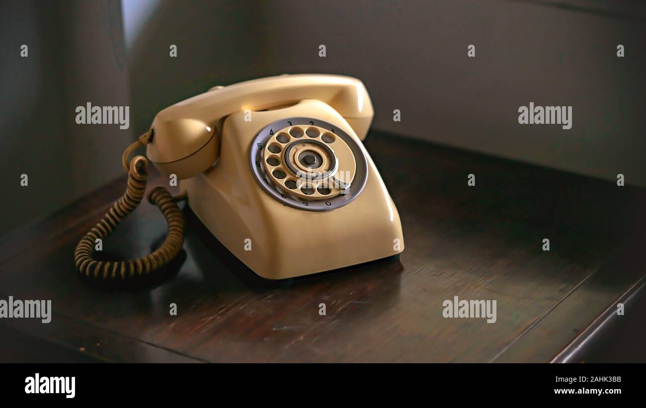 Il vecchio marrone chiaro telefono su marrone woodent tabella nella luce della lampada dello sfondo. Foto Stock