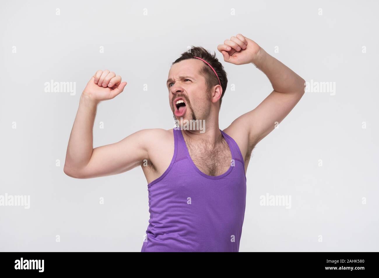 Funny uomo con i baffi che mostra i suoi muscoli su sfondo grigio Foto Stock
