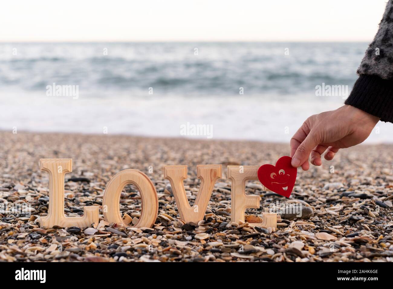 Lettere di legno costituente la parola amore e una mano che regge un cuore rosso sulla riva del mare. concetto di san valentino Foto Stock