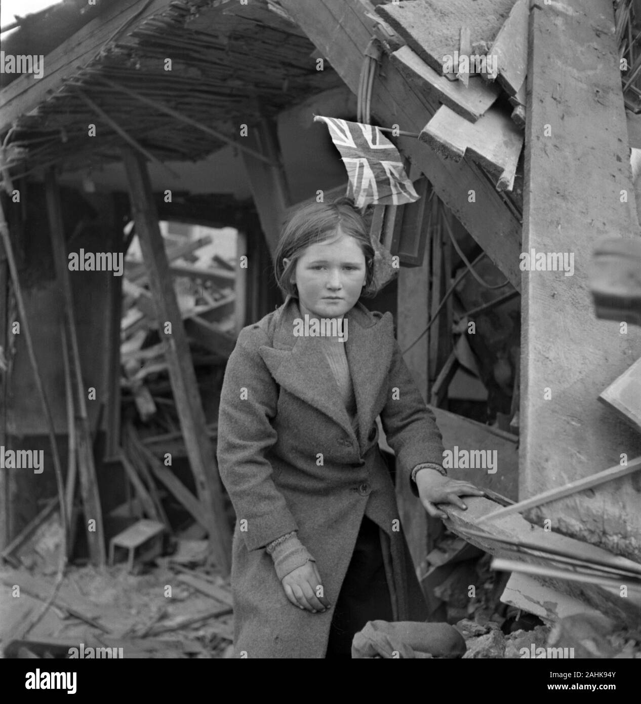 Ragazza in piedi dalle rovine di edificio e battenti bandiera inglese durante la Seconda Guerra Mondiale bombardamenti di Battersea, Londra, Inghilterra, Regno Unito, fotografia di Toni Frissell, Gennaio 1945 Foto Stock