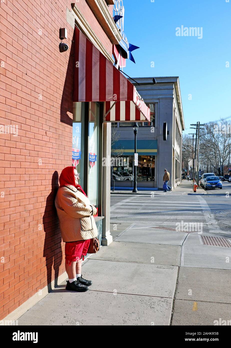 Una donna anziana si erge contro una parete in Ohio città quartiere di Cleveland, Ohio, Stati Uniti d'America prendendo il raro sole invernale. Foto Stock