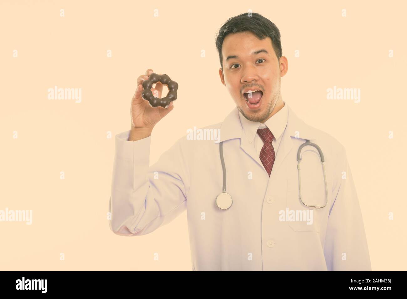 Studio shot di giovani felici uomo asiatico medico sorridente e bocca di apertura mentre si tiene a ciambella Foto Stock