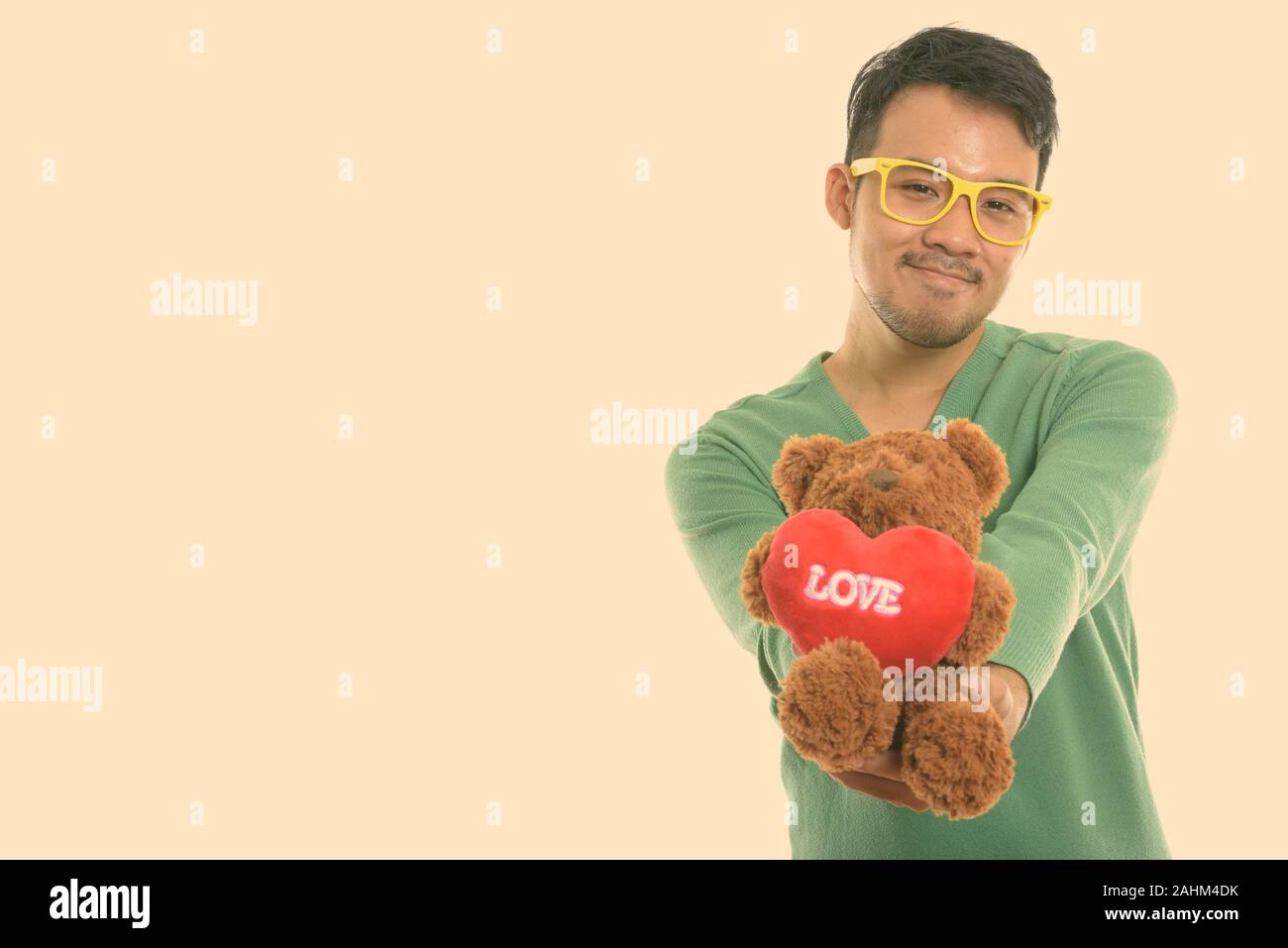 Studio shot del giovane uomo asiatico dando orsacchiotto di peluche con cuore e amore segno Foto Stock