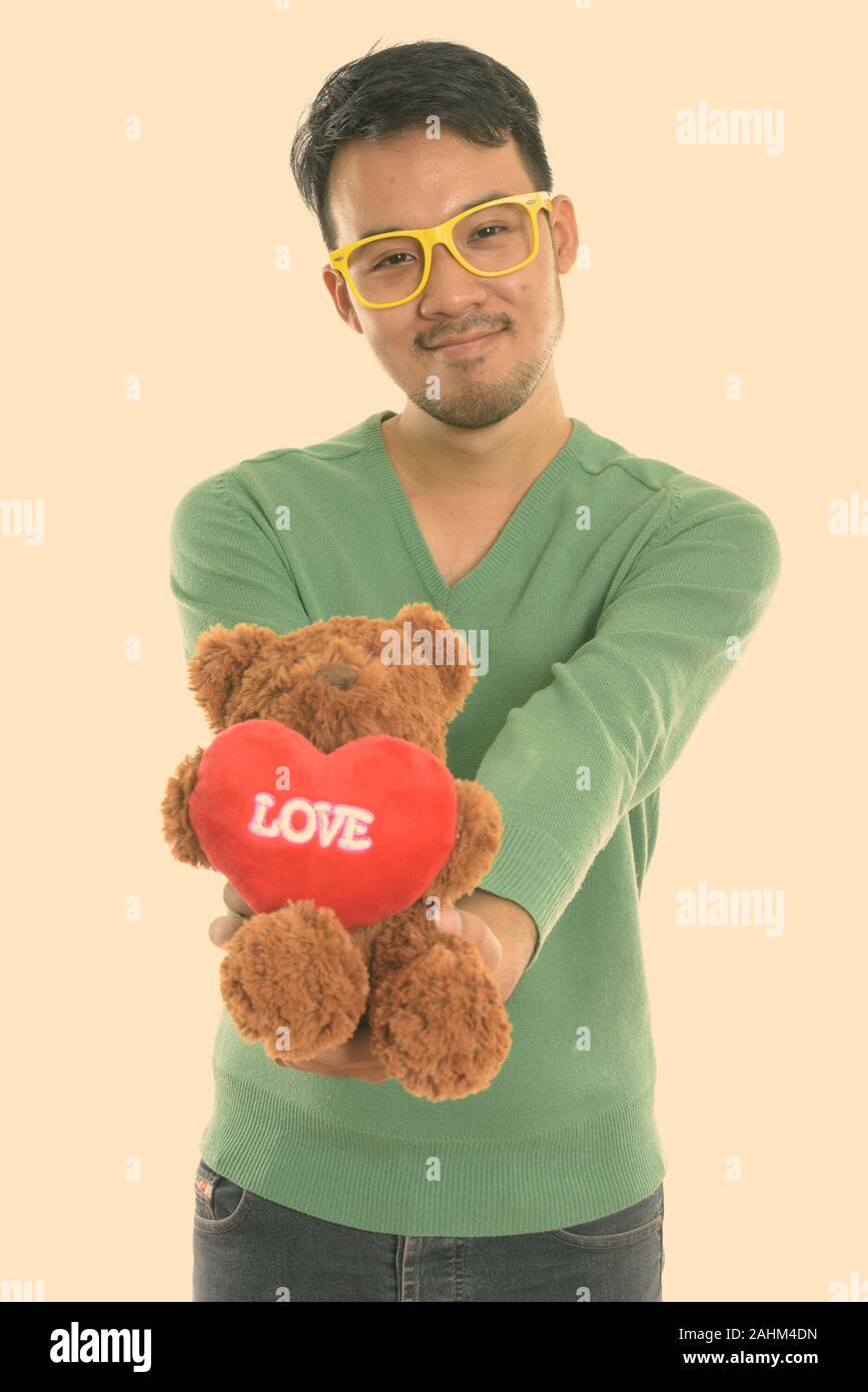 Studio shot del giovane uomo asiatico dando orsacchiotto di peluche con cuore e amore segno Foto Stock