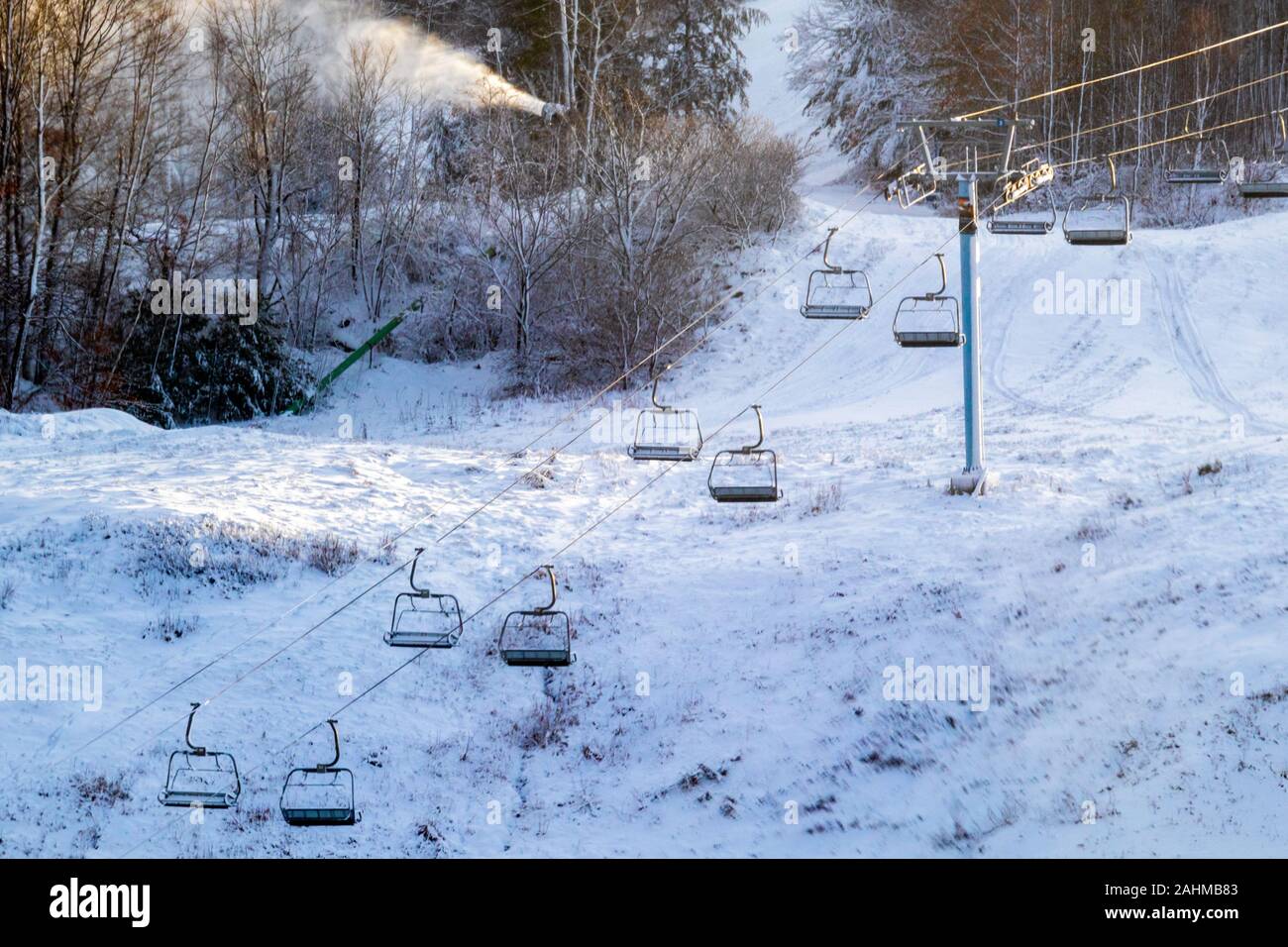 Una seggiovia in esecuzione in salita sul pendio di una collina di sci è fermo in piedi con le sue sedi appeso. La collina sottostante ha bisogno di più la neve e una neve ma Foto Stock