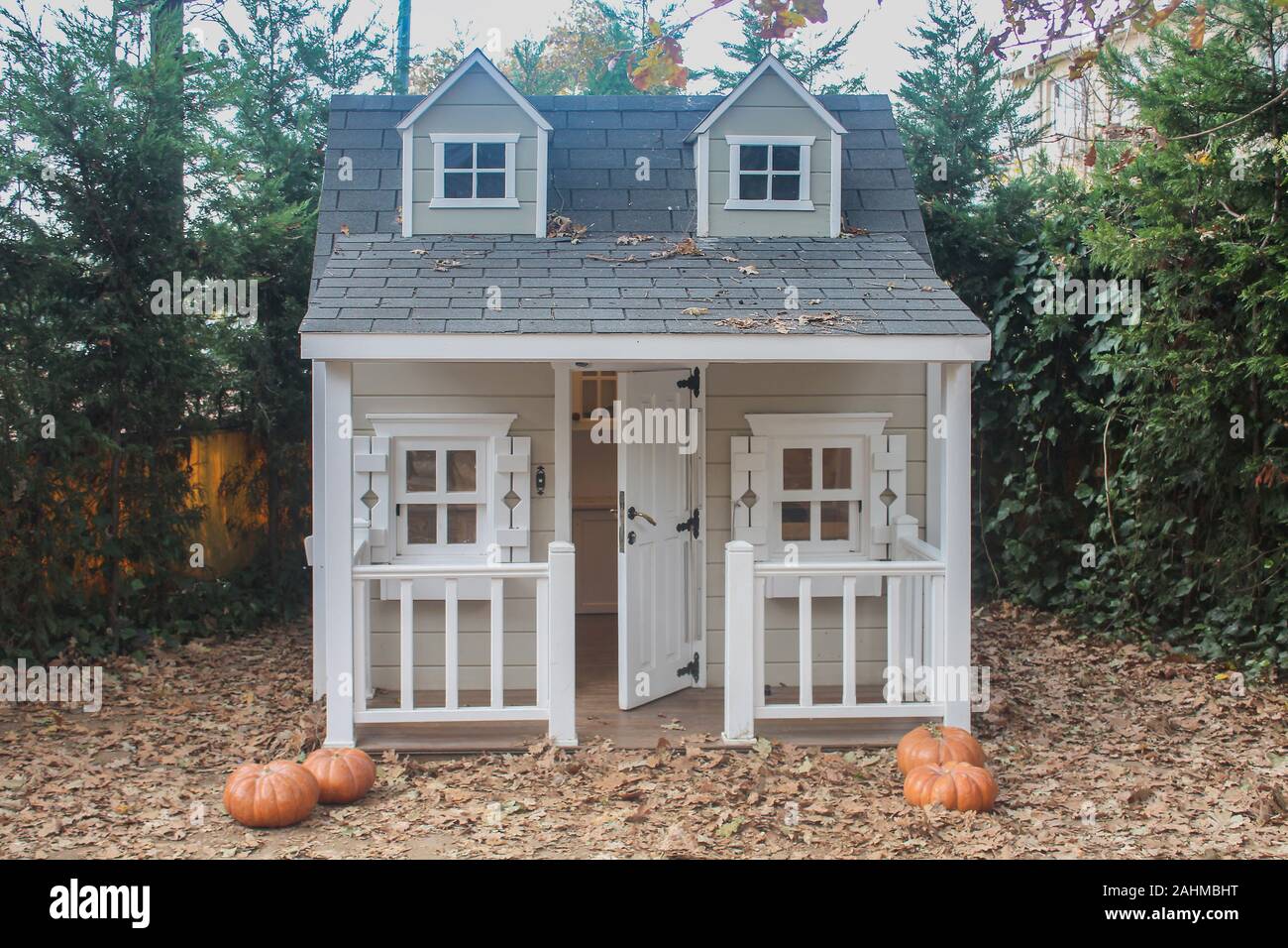 La facciata anteriore di un giocattolo di una casa con un portico, sportello aperto in un giardino con zucche e foglie cadute, a cadere. Foto Stock