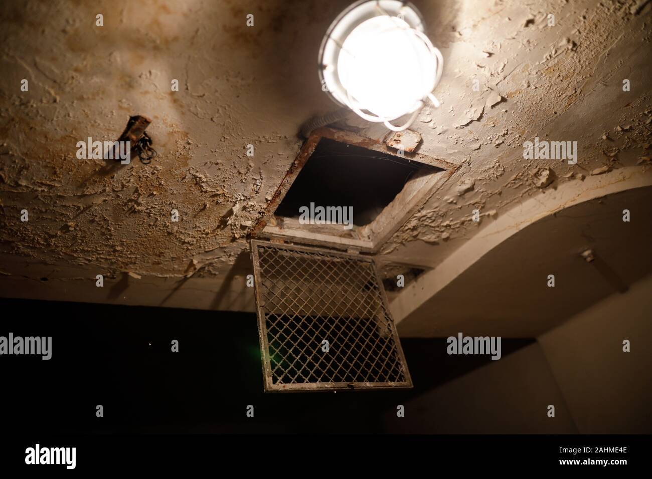 Grungy immagine con la lampadina e una rete metallica su un usurato il soffitto di una vecchia cella di prigione. Foto Stock