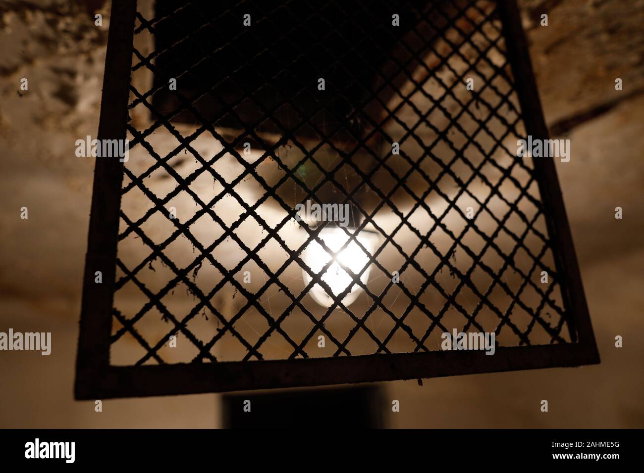 Grungy immagine con la lampadina e una rete metallica su un usurato il soffitto di una vecchia cella di prigione. Foto Stock