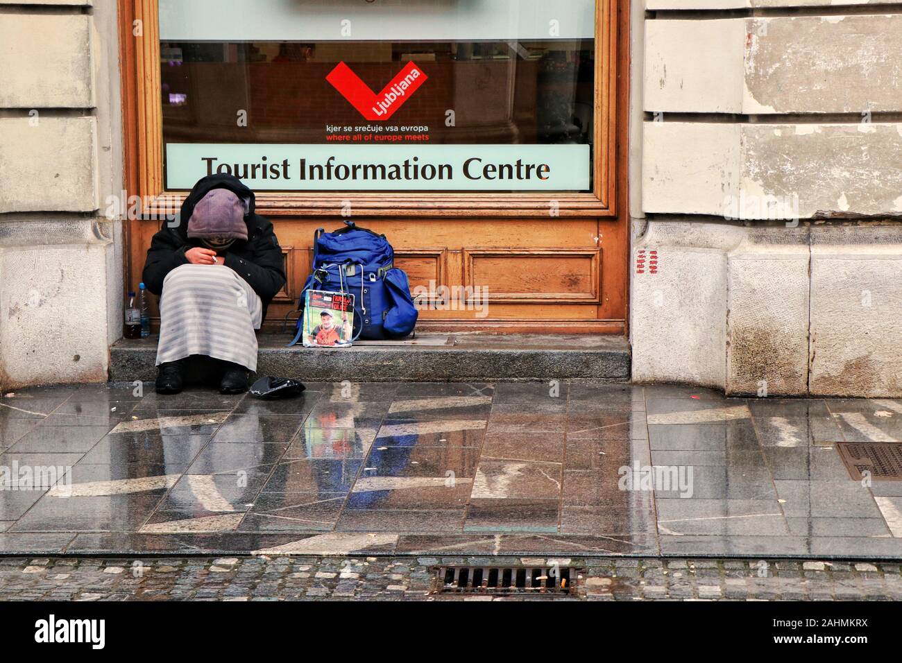 Un uomo senza tetto ripara dalla pioggia al di fuori del centro di informazioni turistiche a Lubiana, capitale della Slovenia. Foto Stock