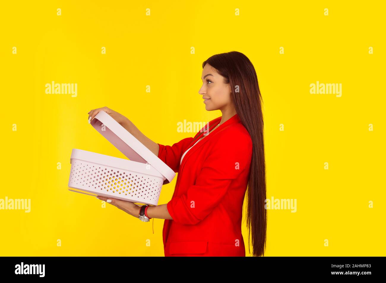 Profilo laterale di una donna che mantiene una scatola aperta. Razza mista modello isolato su sfondo giallo con copia spazio. L'immagine orizzontale. Naturale, nessun trucco. Foto Stock