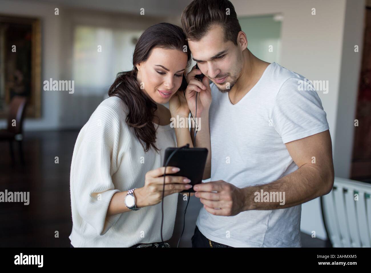 Giovane coppia caucasica l ascolto e la condivisione di musica di tablet e cuffie per interni Foto Stock