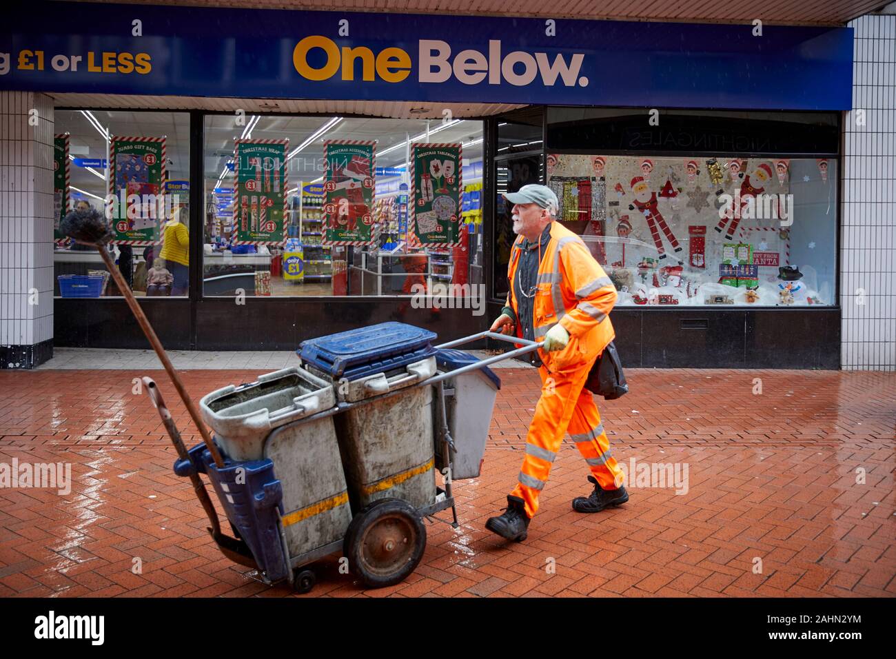 Wrexham in Galles, un pulitore di via passando uno al di sotto di una libbra di negozio o meno Foto Stock