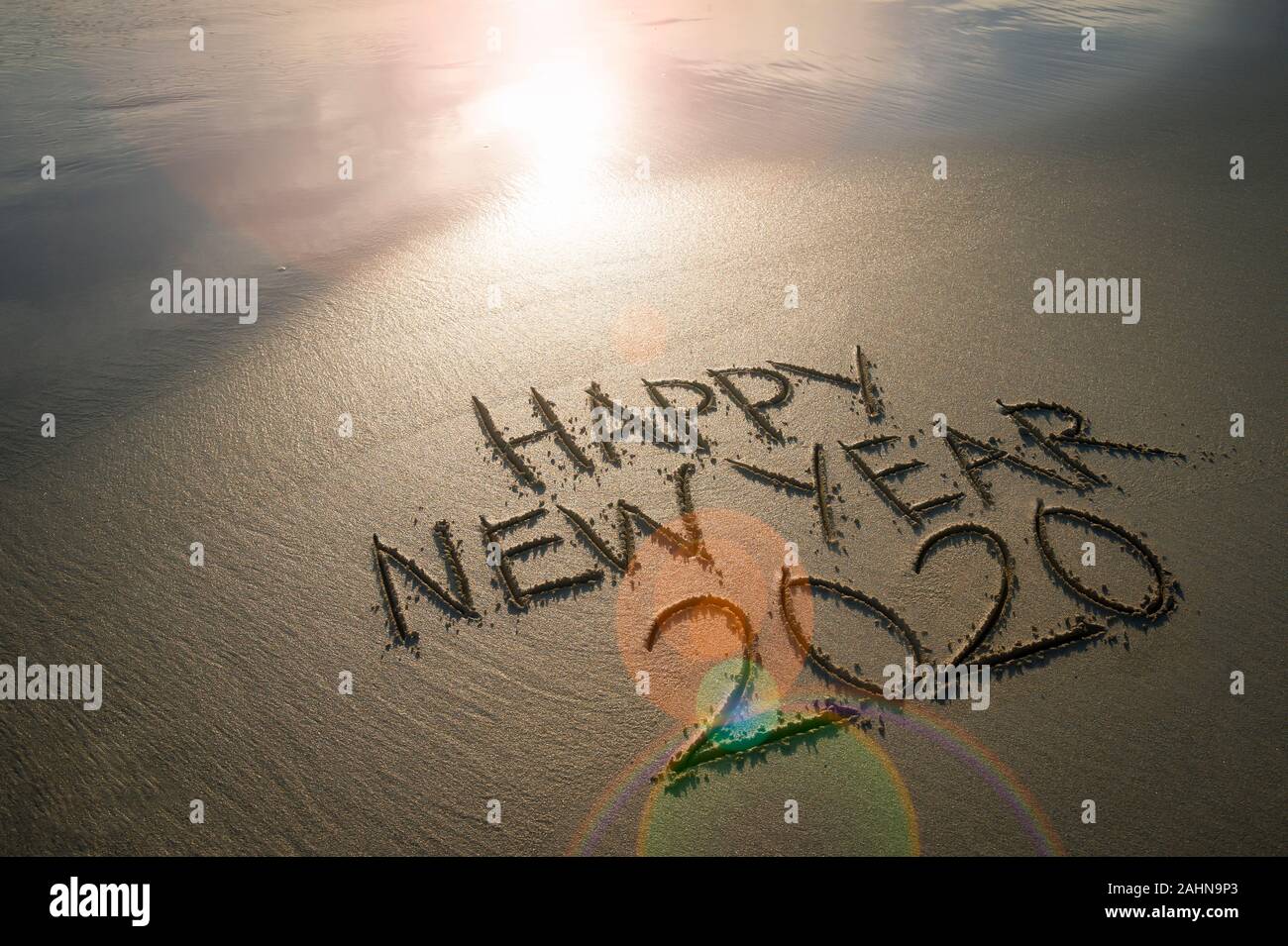 Felice Anno Nuovo 2020 manoscritte del messaggio in sabbia pulita sotto incandescente lens flare sunrise su una spiaggia deserta Foto Stock