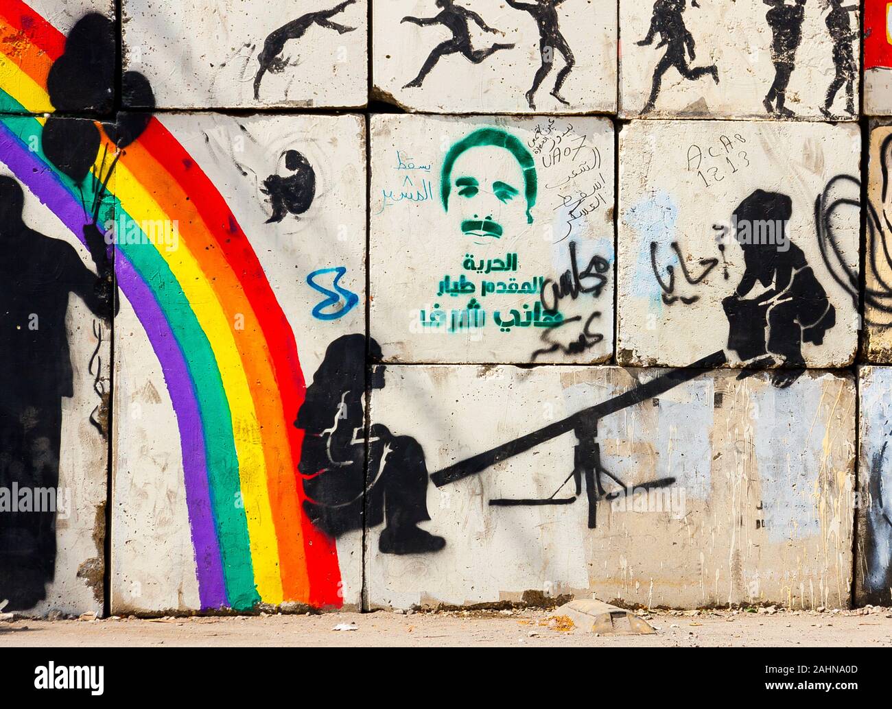 L'Egitto, al Cairo, graffiti di egiziani di rivoluzione su una parete di bloccaggio di una strada adiacente alla sharia Mohamed Mahmoud. I bambini giocano swing nei pressi di un arcobaleno. Foto Stock