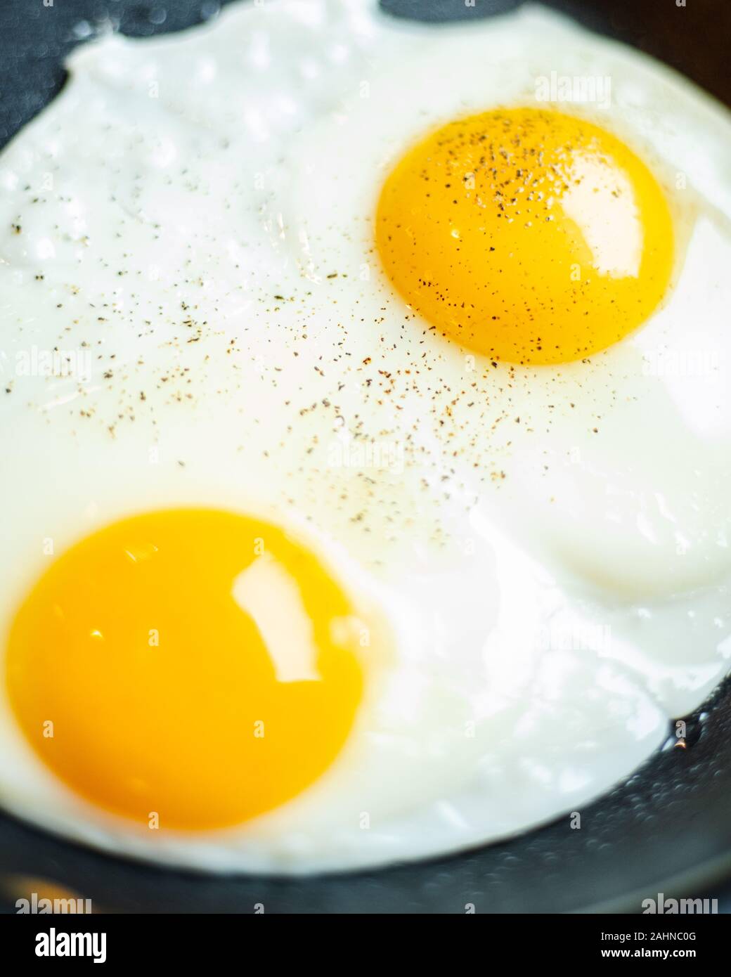 Chiudere la cottura due uova con tuorlo d'uovo in padella di ferro con pepe Foto Stock