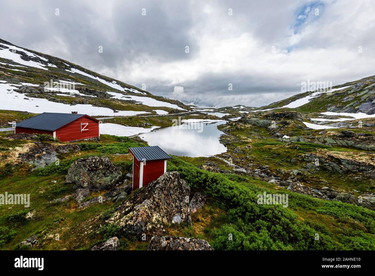 Red capanna in legno e toilette sono nel bordo del lago Galgebergstjornane in Norvegia. La pendenza della collina Galgeberg e il norvegese Country Road 55 sono Foto Stock