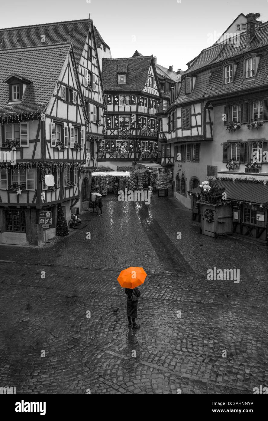 Persona in possesso di ombrello arancione in piedi in Colmar street edito in bianco e nero Foto Stock